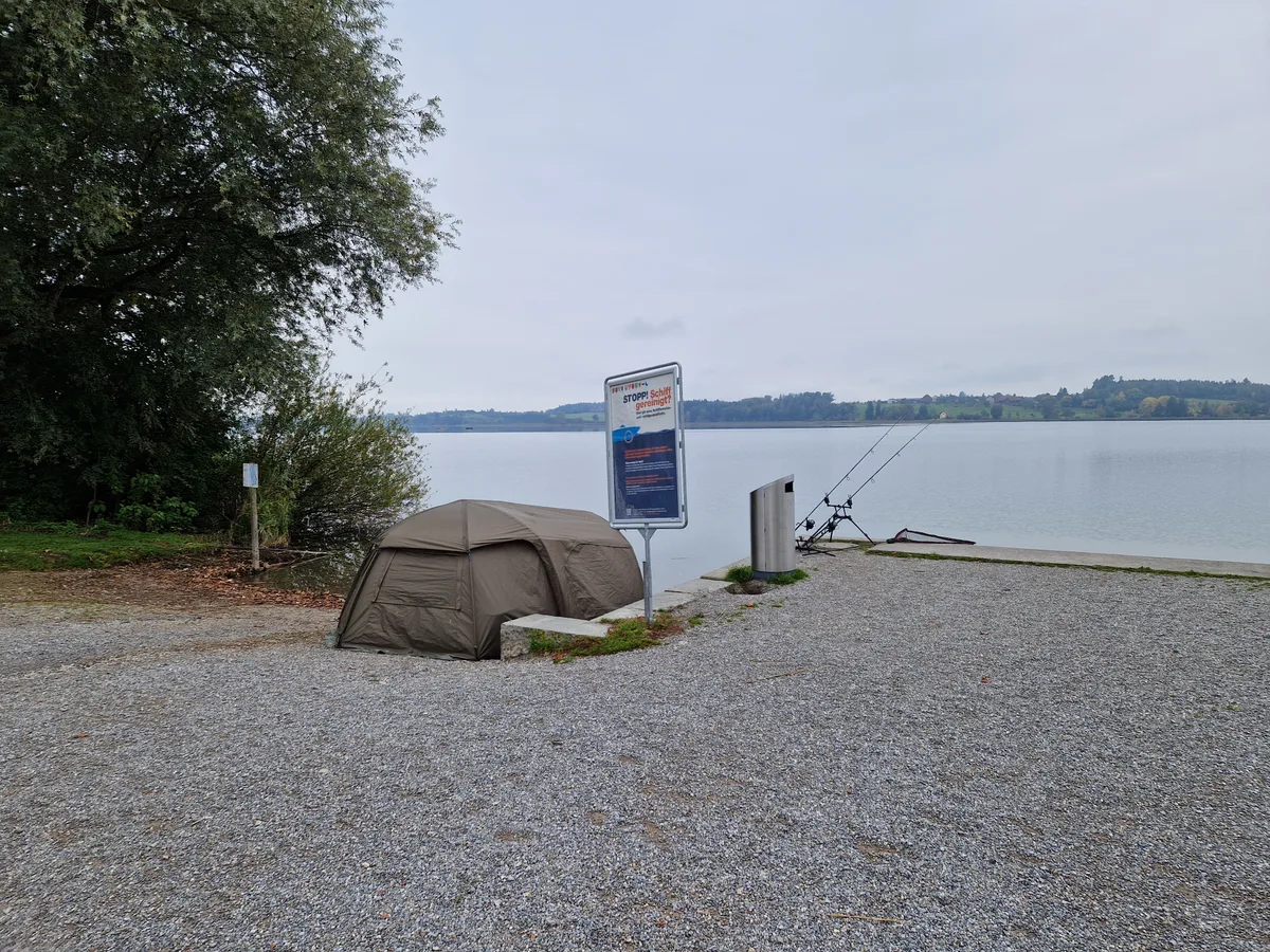 Ein kleines, olivgrünes Zelt steht am Seequai in Pfäffikon. Man sieht zwei Angeln, die vor dem Zelt an der Quaimauer befestigt sind.